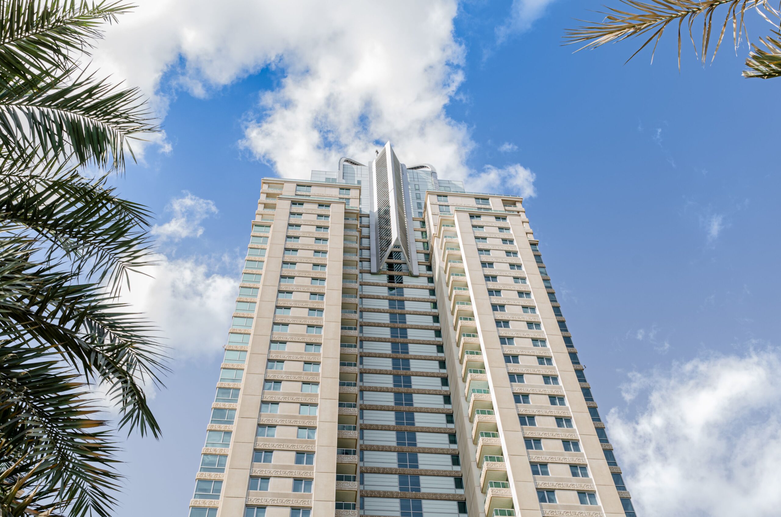 Low-angle view of a modern glass and stone residential tower against a blue sky near The Square Tower, JVC