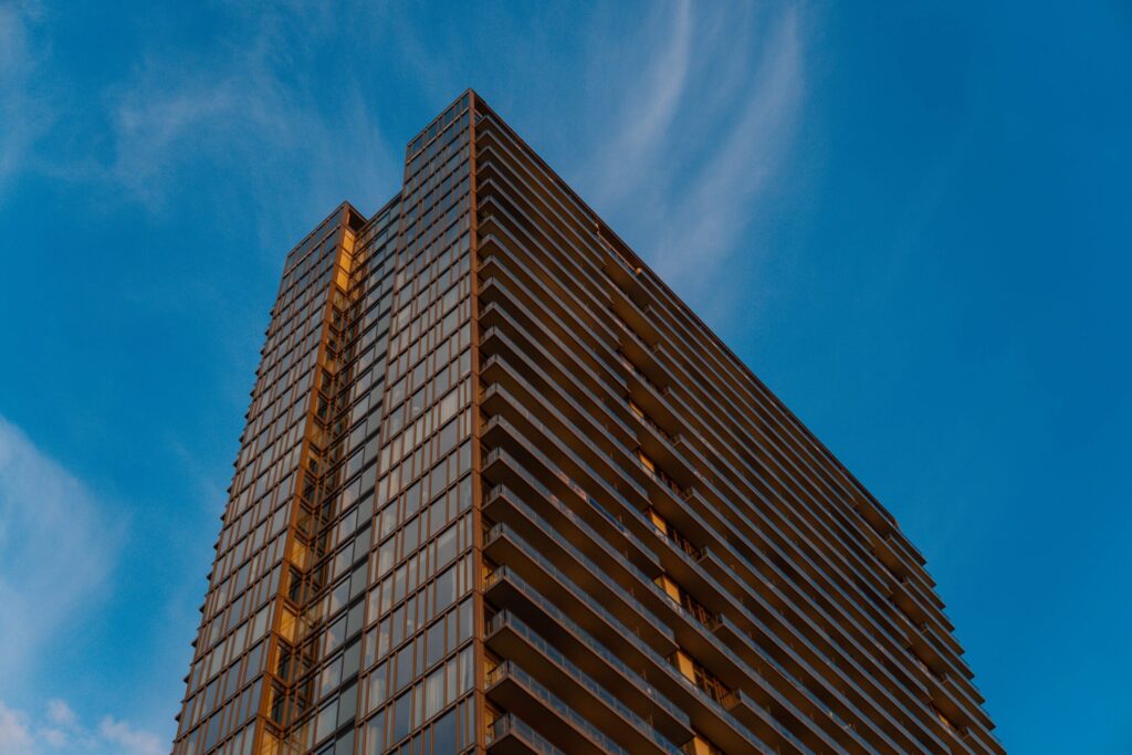 Upward view of a modern glass high-rise tower with staggered balcony bands lit at golden hour, Business Bay