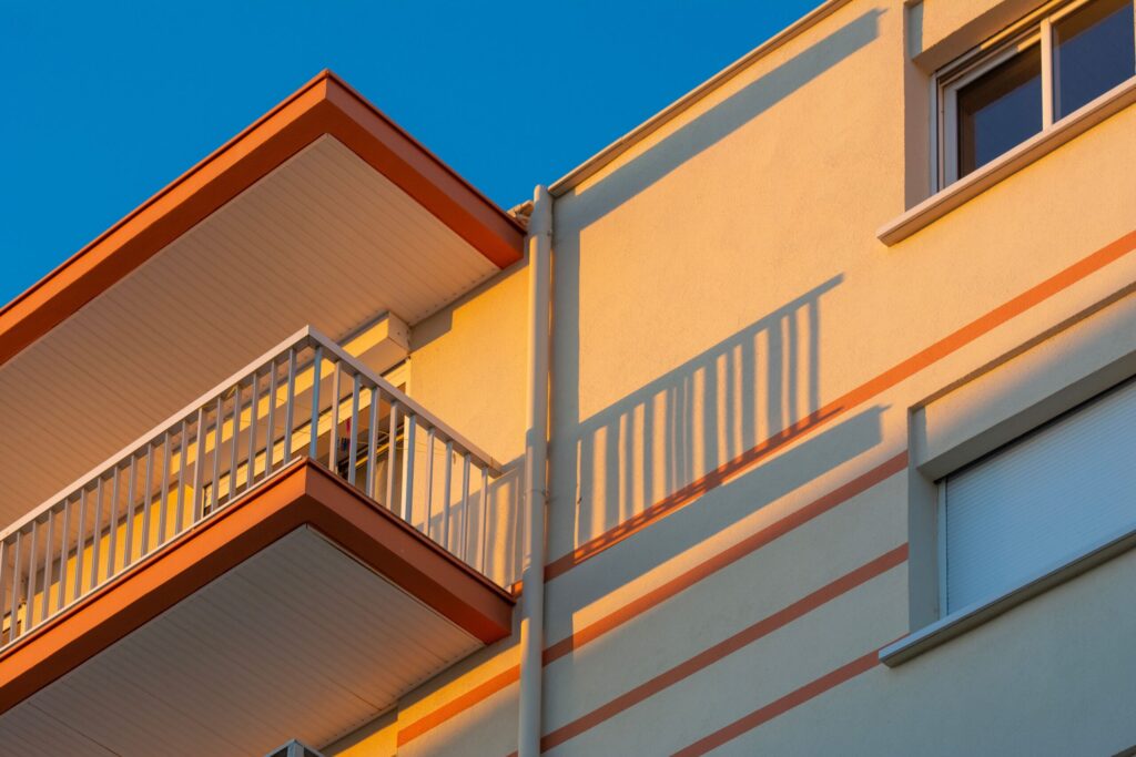 Close-up of a modern apartment facade with orange-trimmed balcony edges and sharp sunlit shadows, representative of Silicon Heights II in Dubai Silicon Oasis, Dubai