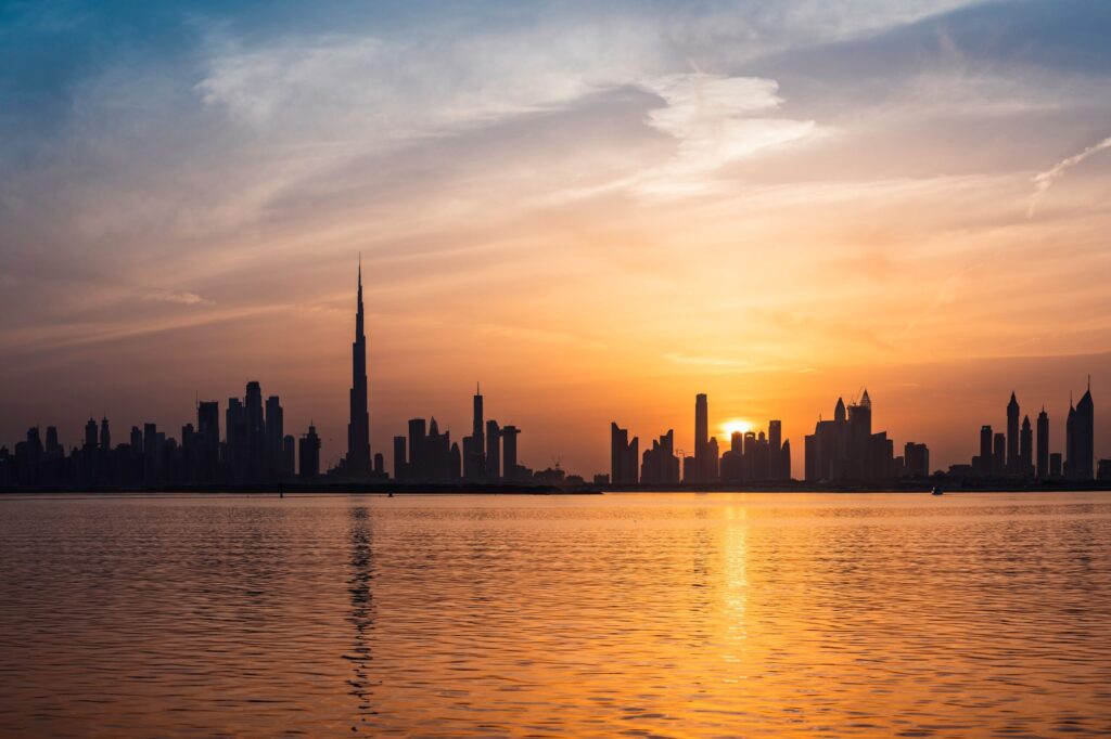 Dubai skyline silhouetted against a sunset with its reflection on the water