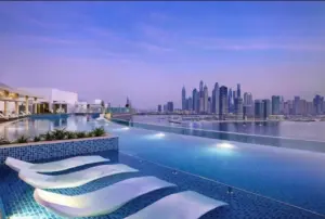 Infinity pool with white sun loungers set in the water, looking across to the Dubai Marina skyline at dusk